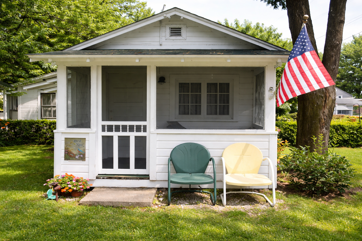 White cottage with screened porch, American flag, and colorful outdoor chairs.