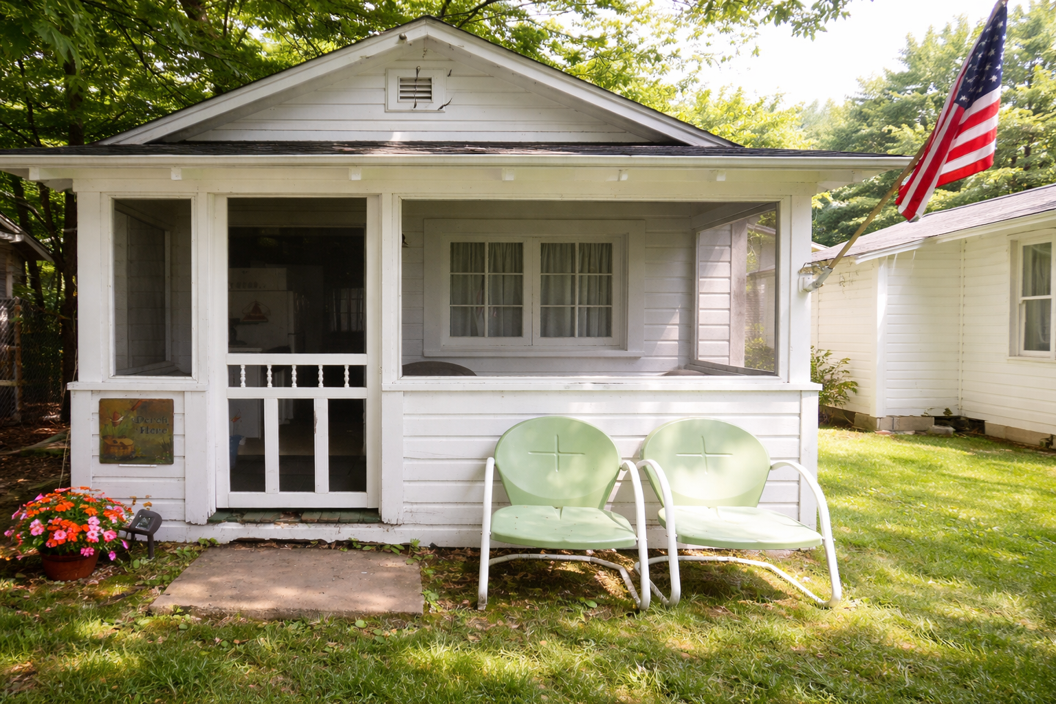 White cottage with screened porch and two green chairs on a grassy lawn.