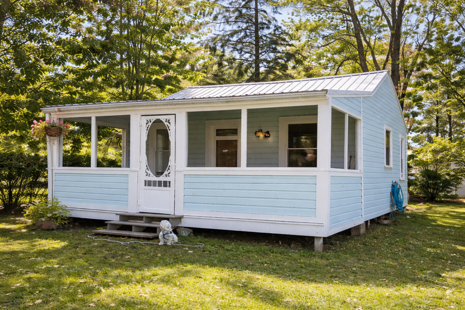 Light blue cottage with screened porch, white trim, and sunny yard with trees.