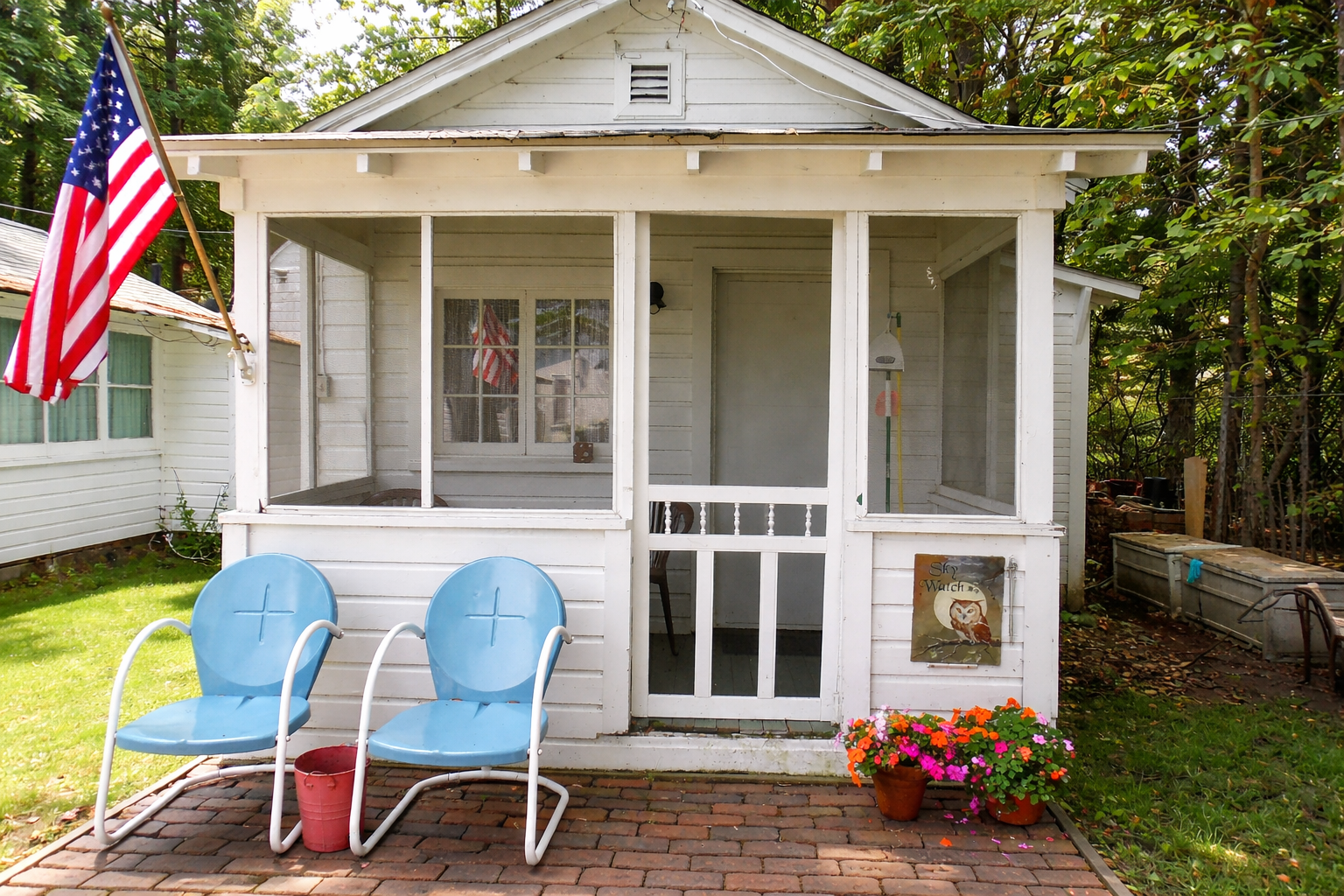 White cottage porch with blue chairs and flower pots in a shaded yard.